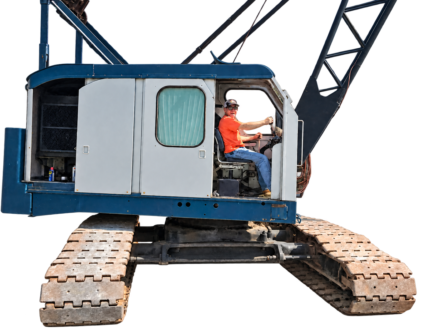Jeff, wearing a cap, sunglasses, and an orange shirt, smiling from the operator’s seat of a crawler crane.